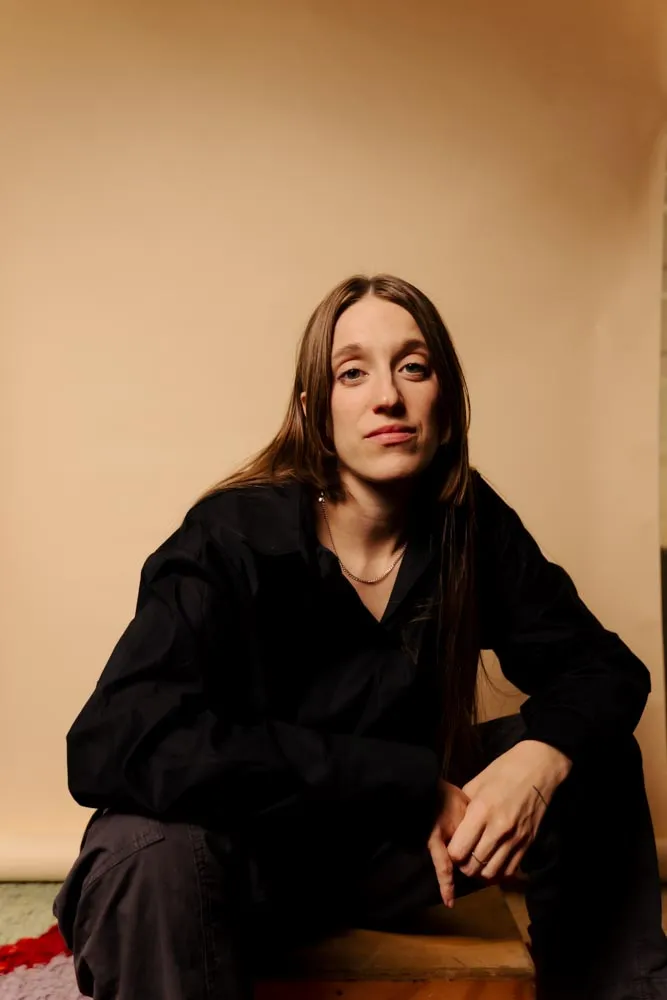 Sara Drake, seated, in a dark shirt against a warm backdrop.